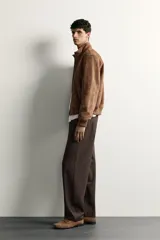 Pantalón chino de corte regular, color marrón oscuro, con cierre frontal de cremallera y botón, bolsillos laterales y bolsillos traseros de vivo.