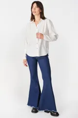 Camisa de color marrón claro, con cuello clásico, cierre frontal de botones y mangas largas con puños ajustados y volumen en los hombros.