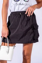 Falda corta negra de material ligero y brillante, con cintura elástica fruncida y bolsillos cargo frontales. El ruedo tiene un efecto abullonado o globo.