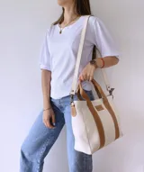 Bolso tipo tote de lona color crudo con detalles en cuero color marrón. Tiene doble asa corta de mano y correa larga de hombro.