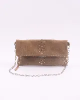 Bandolera de cuero gamuzado color marrón oscuro, con diseño rectangular y solapa frontal decorada con tachas metálicas plateadas. Incluye una cadena metálica plateada larga para usar al hombro o cruzada, y una cadena más corta para llevar como sobre.