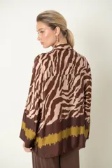 Camisa de manga larga con cuello camisero, corte holgado y estampado de cebra en tonos marrón y negro. Presenta una guarda horizontal con efecto esfumado en negro y marrón en el bajo y puños.
