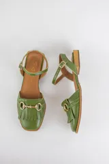 Sandalias de cuero color celeste, con punta cerrada, flecos frontales y detalle de estribo metálico dorado. Tienen tira ajustable al tobillo y suela plana con pequeño taco.