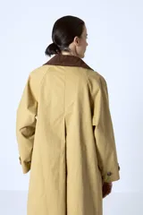 Trench color beige con cuello camisero, doble botonadura frontal, cinturón y bolsillos laterales.