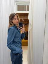 Camisa de denim fino en tono azul medio, con cuello alto con volados, mangas largas con puños con volados y cierre frontal con botones en contraste color rojo.
