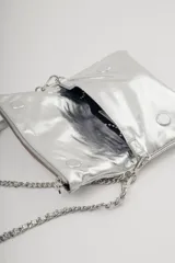 Cartera tipo bandolera de cuero metalizado plateado, con solapa frontal y logo de la marca grabado. Incluye una correa combinada de cadena metálica y cuero, desmontable y regulable.