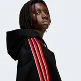 Hoodie Adidas Originals de corte holgado, color negro, con capucha y cordones ajustables. Presenta el logo del trébol bordado en el pecho y bandas laterales en las mangas con rayas rojas y blancas.