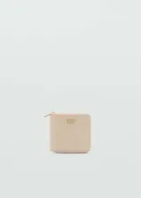 Billetera mediana de efecto piel en color beige, con cierre de cremallera perimetral y placa metálica dorada con el logo de la marca en el frente.