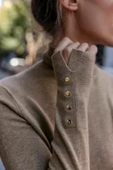 Jersey de punto negro con cuello alto y manga larga, con detalle de botones metálicos dorados en los puños.