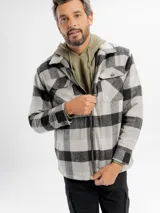 Sobrecamisa de corte recto con estampado de cuadros grandes en tonos gris y negro. Presenta cierre frontal con cremallera, cuello clásico, dos bolsillos frontales con solapa en el pecho y forro interior de sherpa para mayor calidez.