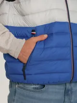 Chaleco acolchado Tommy Hilfiger con diseño triblock en azul marino, gris y azul. Cuenta con cuello alto, cierre de cremallera frontal, dos bolsillos laterales con cremallera y logo bordado en el pecho.