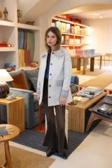 Chaqueta de gabardina color crema con cuello estilo babero, puños y bolsillos con detalle de tela a cuadros en tonos azul, marrón y crema. Presenta cierre frontal con botones y corte recto.