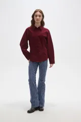 Camisa de pana color marrón, con cuello camisero, cierre frontal de botones y bolsillos en el pecho. Presenta un corte entallado y mangas largas.