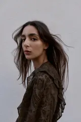 Blusa de manga larga con cuello redondo, confeccionada en tejido semitransparente con estampado paisley en tonos marrones oscuros. Presenta detalles de volantes y apliques de terciopelo en el frente y hombros, con cierre frontal de botones forrados.