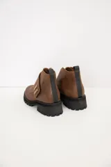 Bota corta de gamuza color chocolate, con suela track dentada y detalle de tira cruzada con apliques metálicos dorados.