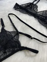 Conjunto de lencería de cuatro piezas en encaje negro. Incluye bralette con breteles regulables, tanga con tiras dobles ajustables en la cintura, portaligas con enganches desmontables y ligas para las piernas.