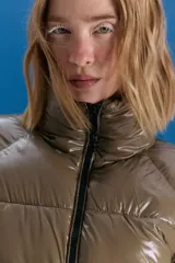 Campera puffer corta a la cintura, color verde militar con acabado brillante. Presenta cuello alto, cierre frontal completo y bolsillos laterales con cierre invisible.