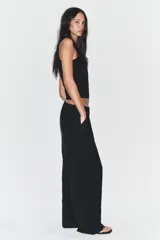 Pantalón negro de tiro alto y pernera ancha, confeccionado en tejido fluido, con bolsillos laterales y detalles de pliegues en la parte delantera.