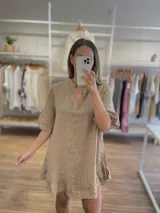 Vestido corto de lino color beige/tostado, con escote en V y cuello mao. Presenta mangas cortas abullonadas y un ruedo con volado.