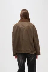 Campera de estilo encerado color marrón, con cuello de pana en tono contrastante, cierre frontal con cremallera y botones a presión, y bolsillos laterales. Presenta un diseño holgado con forro interior a cuadros.