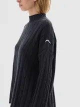 Buzo tejido de punto color beige, con cuello subido, diseño oversized y aberturas laterales en el ruedo.