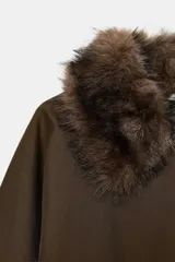 Trench corto de corte recto con capucha y cuello desmontable efecto pelo. Presenta cierre frontal con botones, bolsillos laterales y mangas largas con trabillas en los puños.