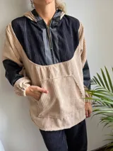 Canguro de pana color beige con capucha, mangas largas de cuero sintético negro y cierre frontal parcial con cremallera.