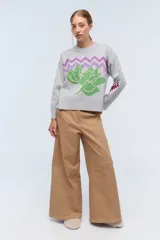 Sweater color camel de tejido de punto con cuello redondo y mangas largas. Presenta bordado de flor en el frente y la palabra 'Rebels' en la manga.