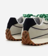 Championes de estilo retro inspirados en botines de fútbol, con capellada de poliuretano en color beige y detalles en azul marino. Presentan suela tractorada color caramelo, refuerzo en el talón y cordones combinados en gris y verde.
