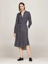 Vestido camisero midi azul marino con estampado geométrico en blanco, cuello camisero, manga larga con puños abotonados, cierre frontal con botones, cinturón de lazo y bajo asimétrico.