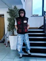 Chaleco puffer negro con capucha, estampado de manos rojas y logo bordado. Cuenta con cierre frontal y bolsillos con cierre.