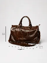 Bolso de viaje color marrón, confeccionado en cuero vacuno, con doble asa de mano y correa ajustable y desmontable. Cuenta con herrajes metálicos y costuras reforzadas.