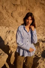 Camisa celeste de silueta entallada con diseño estilo corset, alforzas estructuradas en el torso, cuello clásico, botones oscuros y mangas largas abullonadas.