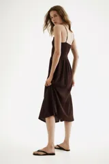 Vestido midi marrón con efecto arrugado, escote cuadrado, breteles finos ajustables y cuerpo elástico en punto smock. Presenta costura fruncida en la cintura y falda con vuelo.