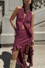 Conjunto de dos piezas color bordó, compuesto por un top halter con escote en V y ajuste elástico en la cintura, y una falda midi con volados laterales y terminaciones desflecadas.