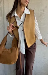 Chaleco de gamuza color camel con bordes decorativos en punto festón de color marrón oscuro. Presenta un diseño sin mangas con escote en V y cierre frontal abierto.