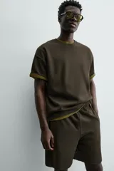 Bermuda de hombre color verde oscuro, de corte relajado y tiro medio. Confeccionada en tejido texturado, presenta cintura elástica con cordón de ajuste interno y bolsillos laterales y trasero de vivo.