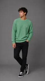 Buzo de punto color verde, con cuello redondo, mangas largas y puños acanalados. Presenta un pequeño bordado en el pecho.