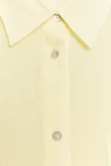 Camisa de corte oversize confeccionada en tejido de gasa color amarillo claro. Presenta cuello solapa, cierre frontal con botones, manga larga con hombro caído y puños definidos, además de un bolsillo de plastrón en el frente y detalle de pinza en la espalda.