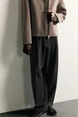 Pantalón de corte balloon fit en color gris oscuro, confeccionado en tejido con viscosa. Presenta pliegues frontales, cintura ajustable con cinturón integrado, bolsillos laterales y bolsillos traseros de doble vivo. Cierre frontal con cremallera y botón.