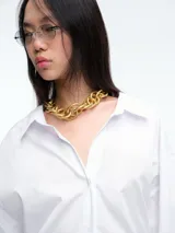 Camisa de corte recto y líneas clásicas, color blanco, con cuello camisero, cierre frontal de botones y puños anchos con botón.