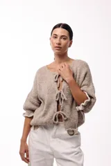 Saco de punto gris con frente abierto, cierre mediante lazos frontales y mangas con puños elásticos. Presenta una textura suave y un diseño de volumen holgado.