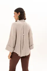 Camisa de textura plisada en color beige, con cuello clásico, cierre frontal de botones y mangas tres cuartos con puños vueltos.