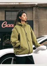 Campera impermeable de color verde pistacho, con capucha ajustable, cierres negros en el frente y bolsillos, y velcro regulador en los puños.