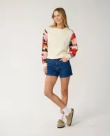 Buzo de cuello redondo color off white, con mangas largas estampadas con diseño patchwork multicolor en tonos rojos, rosas y negros.