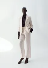 Blazer de lino color beige, de diseño recto con cuello en V, solapas con muesca, mangas largas, bolsillos de ribete delanteros y cierre frontal de un botón.