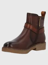 Bota corta de cuero vacuno color marrón con acabado envejecido, presenta una tira decorativa con hebilla metálica en el tobillo y una suela de plataforma de goma texturizada.