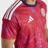 Camiseta de fútbol Adidas de la selección de Costa Rica, modelo Primera Equipación 26. Diseño principal en rojo con estampado abstracto en tonos morados/rosados. Presenta cuello redondo en azul marino y las tres bandas de Adidas en los hombros en blanco. Incluye el escudo de la federación costarricense.