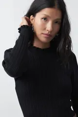 Polera de tejido acanalado color negro, con cuello alto y puños con terminación de volados. Presenta un diseño entallado y textura vertical.
