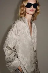 Blazer de estilo oriental confeccionado en hilatura de viscosa con tejido jacquard tono sobre tono. Presenta escote en pico, manga larga y cierre frontal cruzado con alamares a tono.